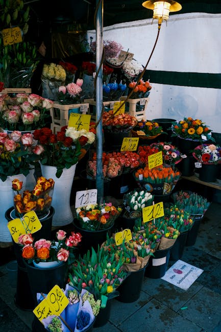 A display of fresh floral arrangements at an outdoor flower market, featuring a variety of colorful flowers including pink and white roses, orange tulips, yellow and purple daisies, and multicolored m