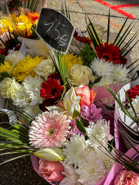 A vibrant floral arrangement displayed outdoors, featuring a mix of fresh flowers including pink gerbera daisies, white roses, yellow chrysanthemums, red gerbera daisies, and pink lilies, all arranged